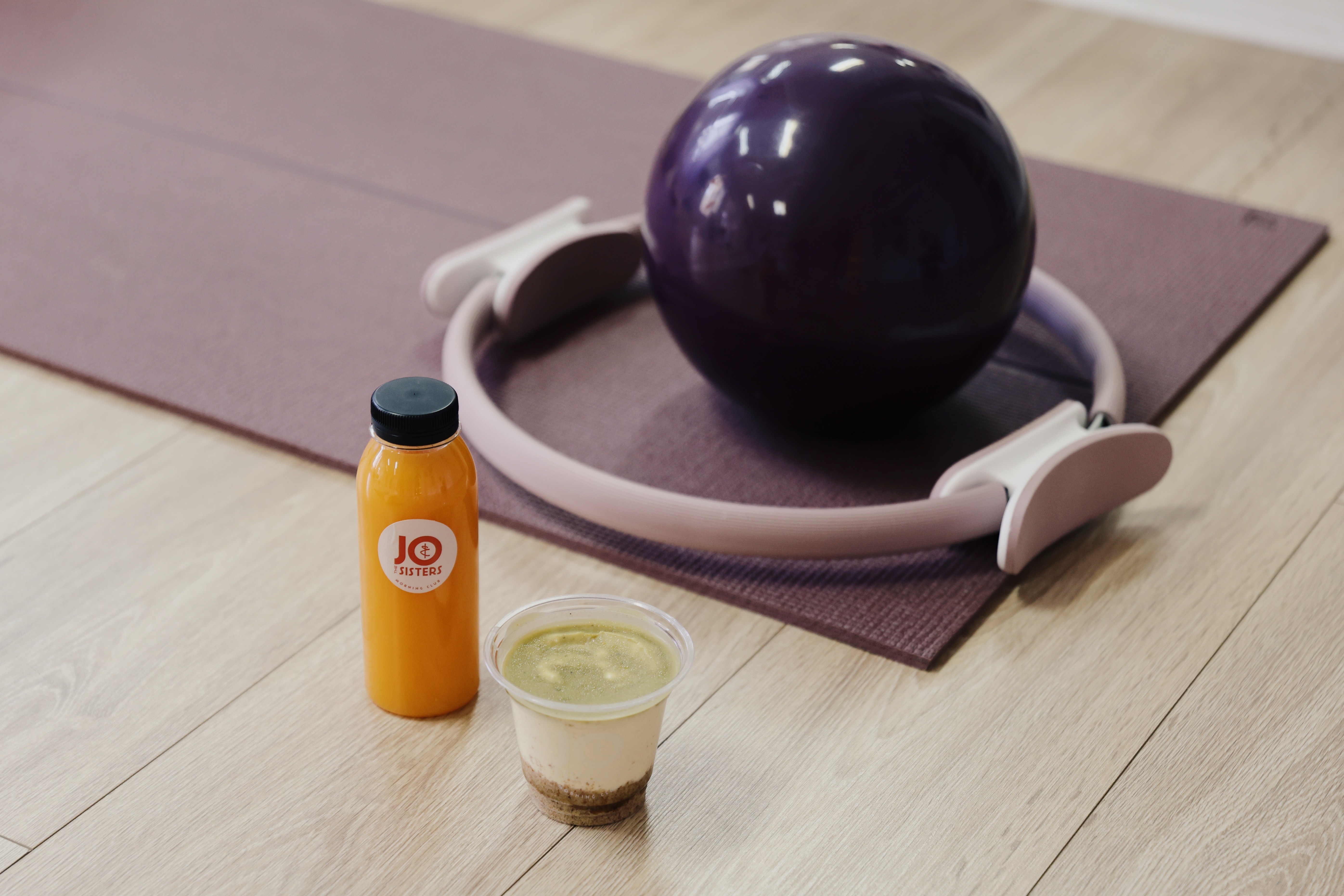 Healthy smoothie and juice placed on a workout mat next to a Pilates ring and exercise ball, representing a nutritious pre- or post-workout breakfast.