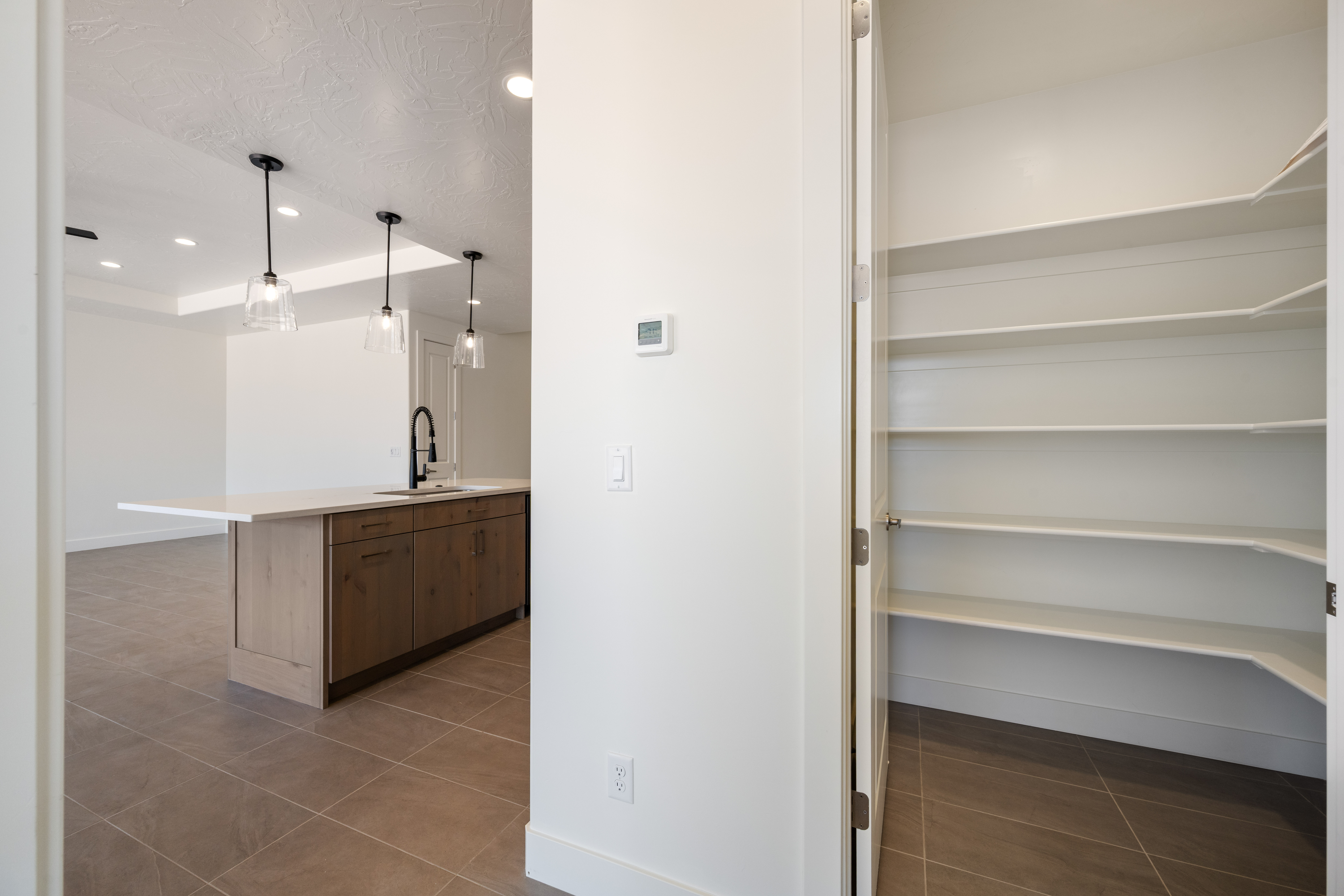 Pantry storage with custom shelving in The Nest at Falcon Ridge, Hurricane, Utah, showing a peek of the adjacent kitchen cabinetry and countertop.