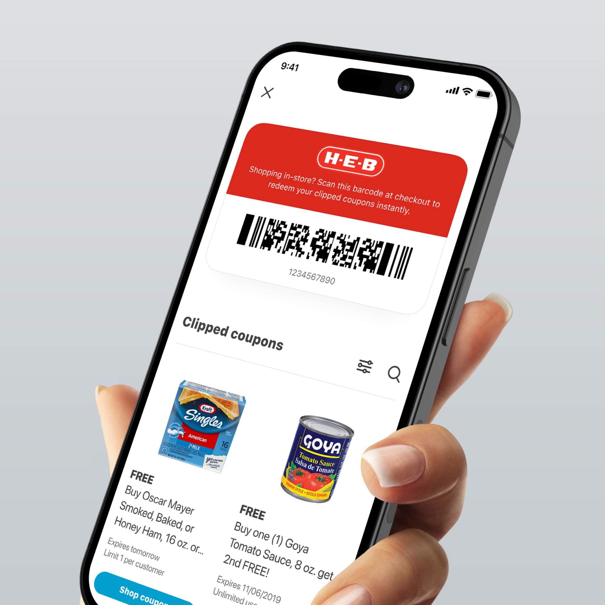 Hand holding a smartphone displaying the H-E-B app with a barcode for redeeming coupons and a list of clipped coupons.