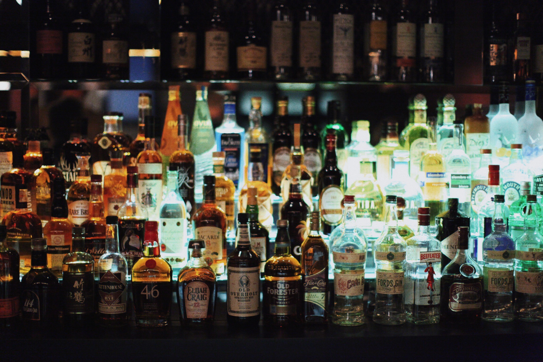 Rows of liquor bottles backlit behind a dark bar.