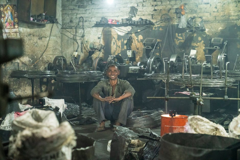 A worker sits happily in a rustic factory surrounded by machinery and wires.