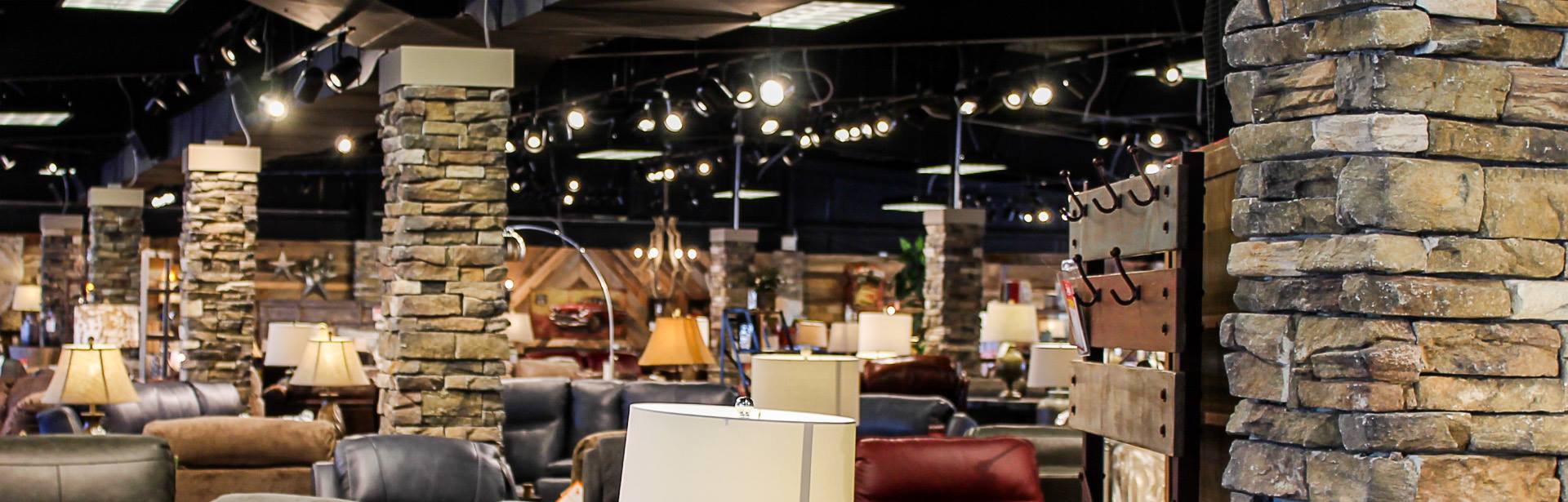 Furniture showroom with stone columns filled with display furniture and home decor items with warm overhead lighting.