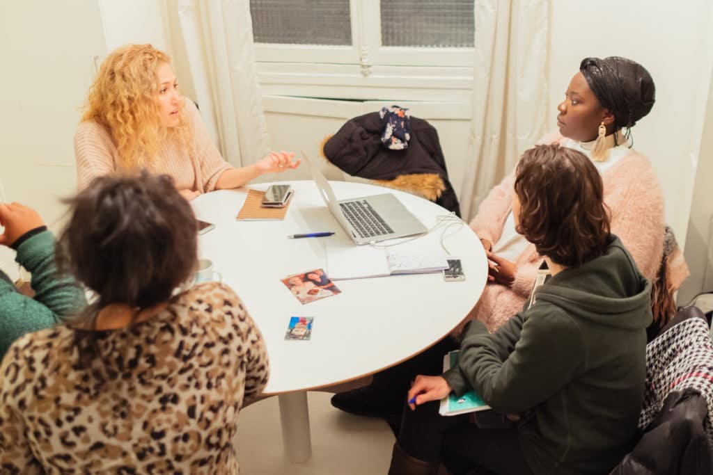 Cinq auxiliaires de vie en réunion autour d'une table ronde, un ordinateur portable ouvert entre elles