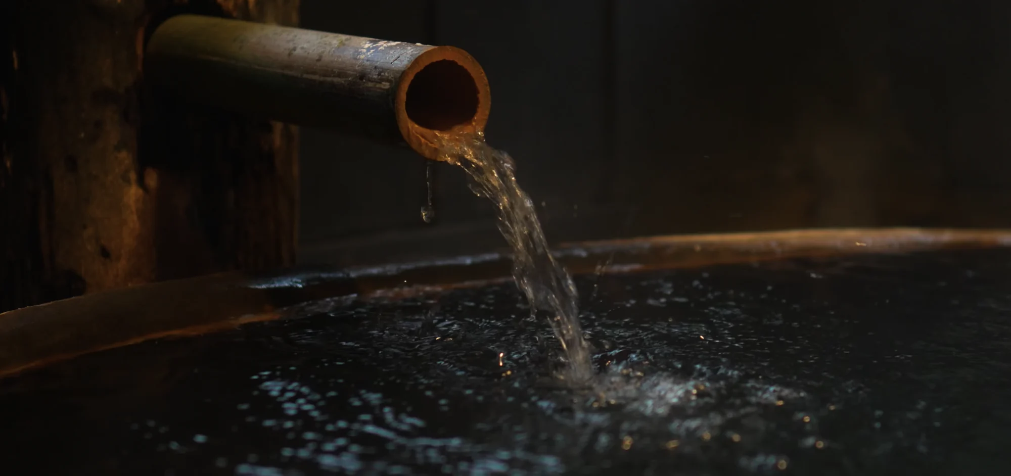 A bamboo spout pouring hot spring water into a round wooden bath tub