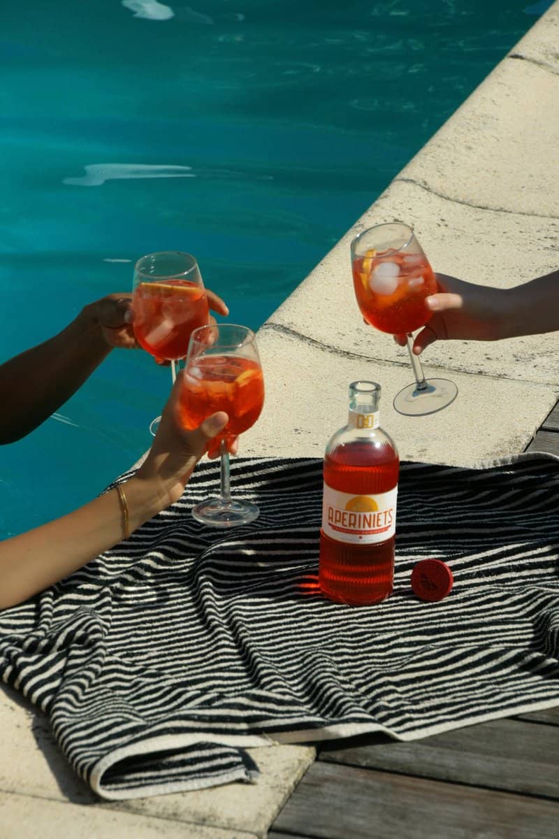 Poolside scene with premium spirits packaging; bottle with decorative closure beside three cocktail glasses.