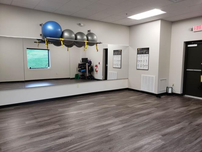 A spacious workout space with wooden floors, a large mirror, and a screen on the wall, featuring minimal decor.
