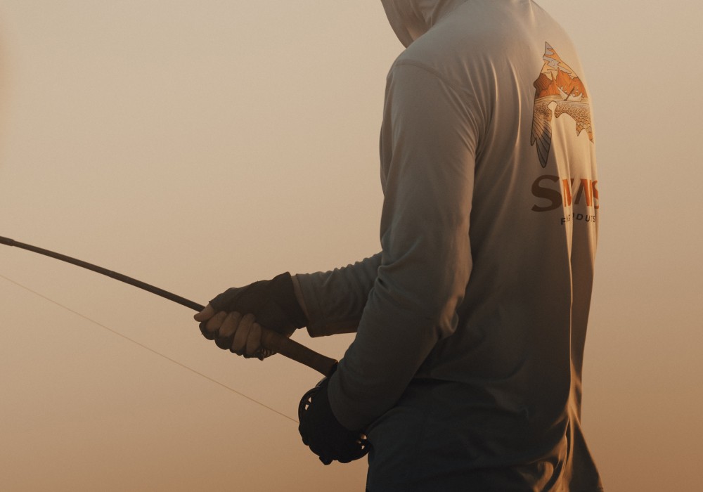 Saltwater angler holding a fly rod and reeling in a fish during golden hour