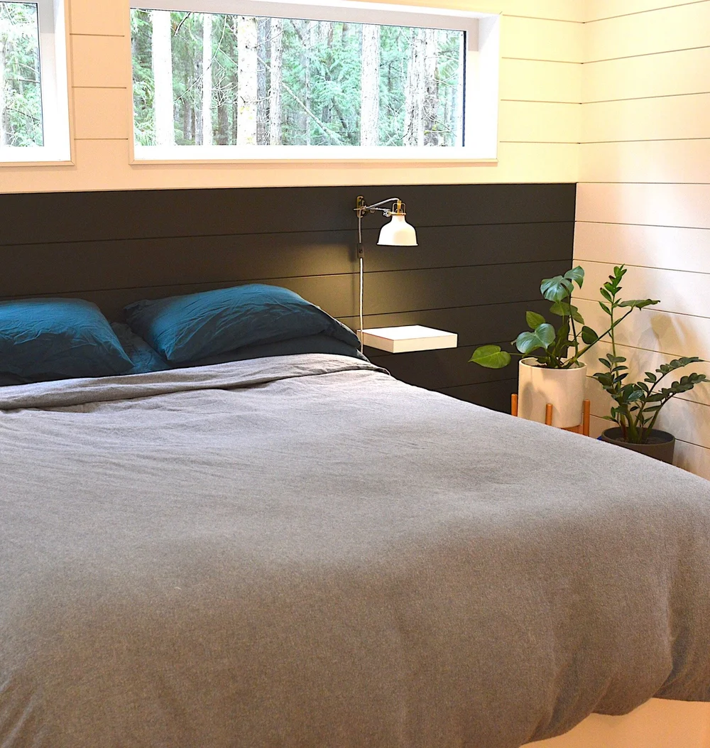 Modern two-story home with large glass windows, warmly lit interiors, and a balcony. Surrounded by trees and a manicured lawn at dusk. Cozy ambiance.