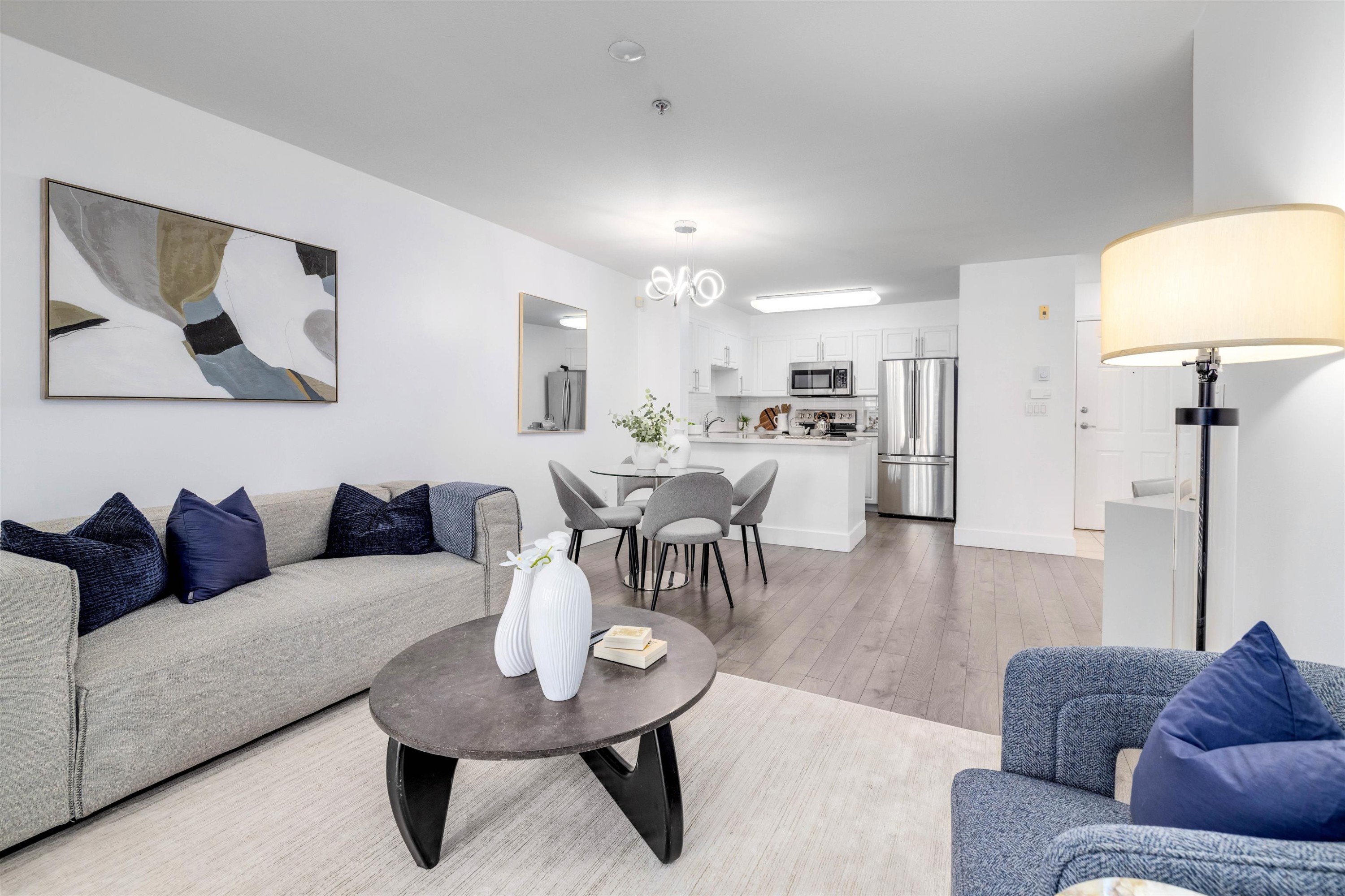 A modern living room with a gray sofa, blue cushions, a coffee table, and a dining area in the background.
