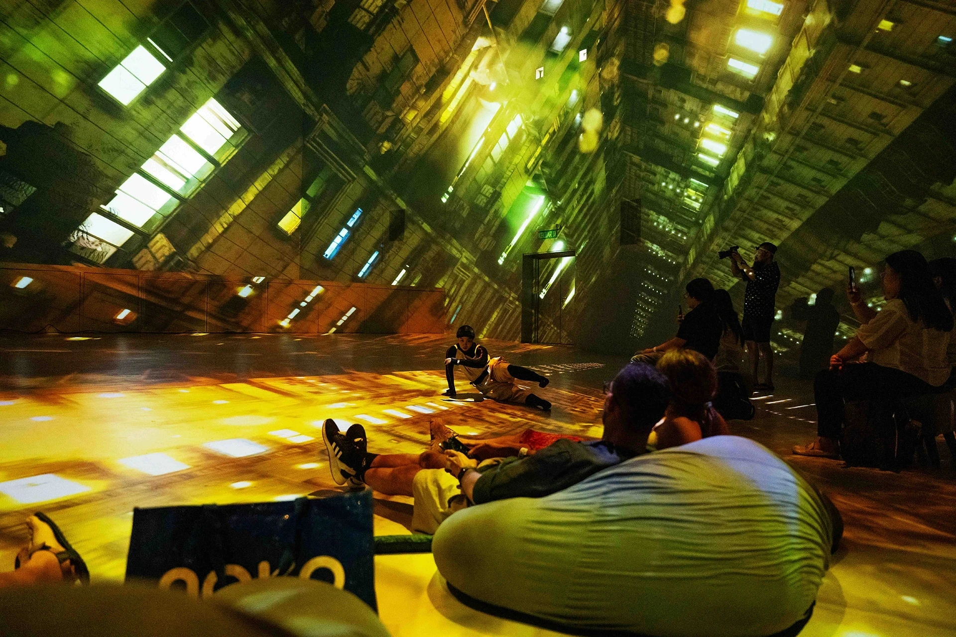 Illuminated abstract projection on walls and floor, people watching.