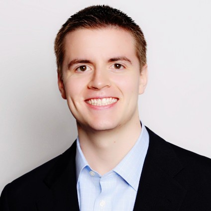 A person with short brown hair looks confidently at the camera, wearing a light pink blazer and white shirt. Soft lighting and plant in the background add a calming tone.