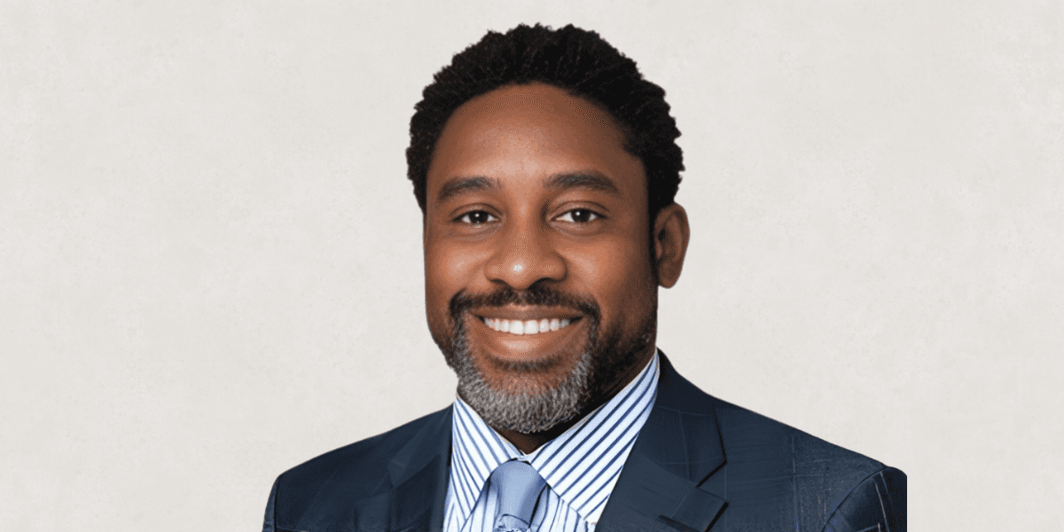A smiling Black man in a suit and tie, representing resilience and success in his professional journey.