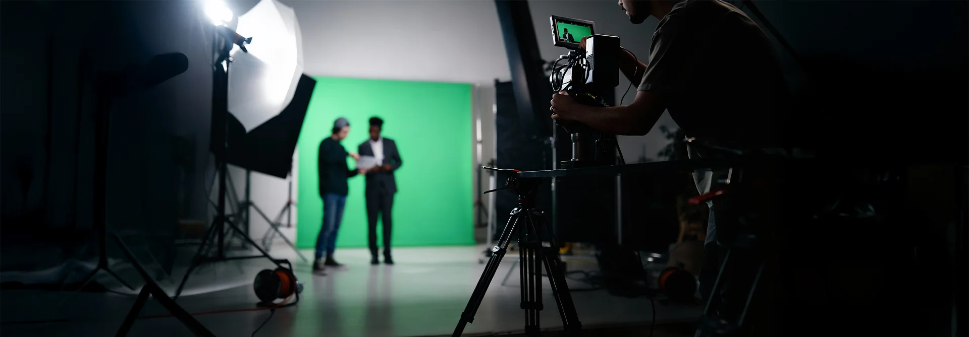 Camera operator filming presenters on a studio set with green screen, lights and equipment prepared for professional video production.