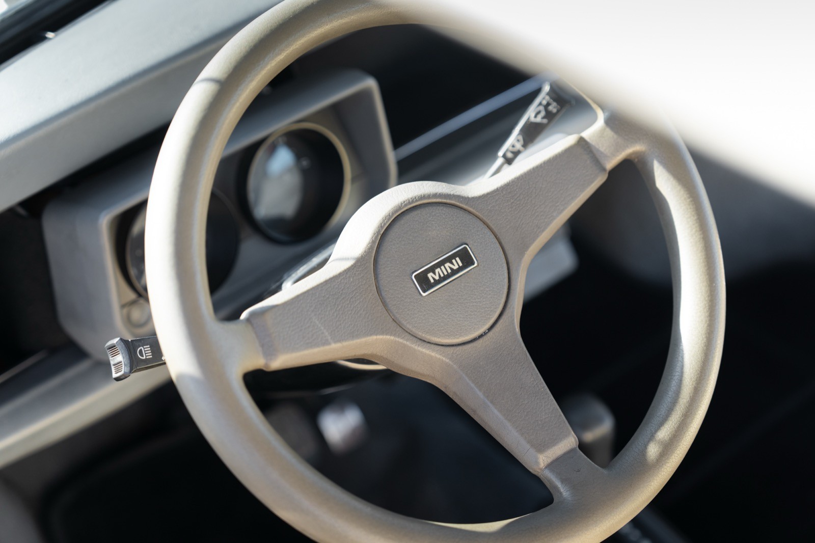 Close-up of a car steering wheel with a silver finish and mounted controls on the dashboard visible in the background.