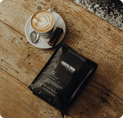 A Flat White coffee in cup on saucer next to a bag of The Coffee Shop blend of coffee