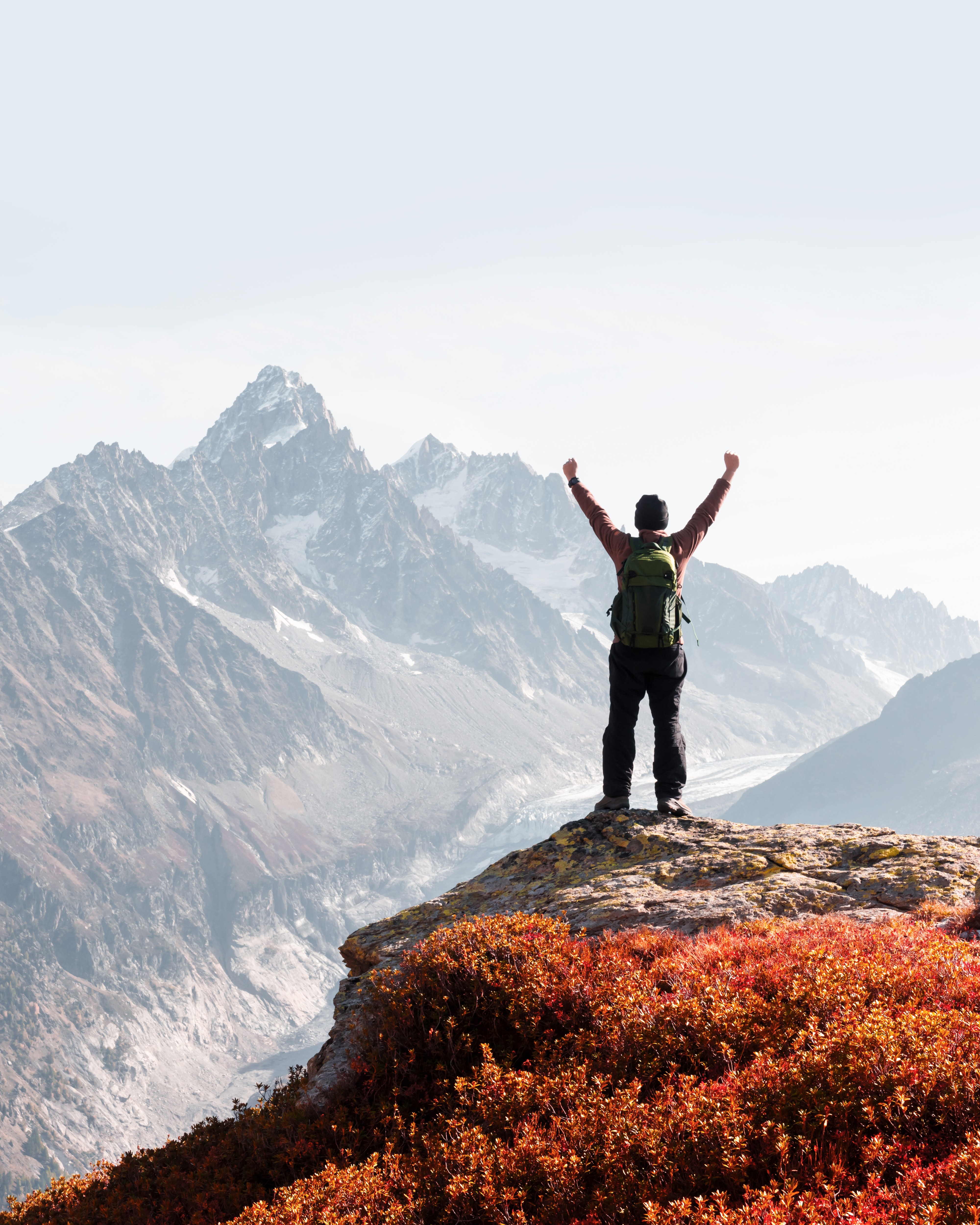 A hiker celebrates at the top of a mountain trail