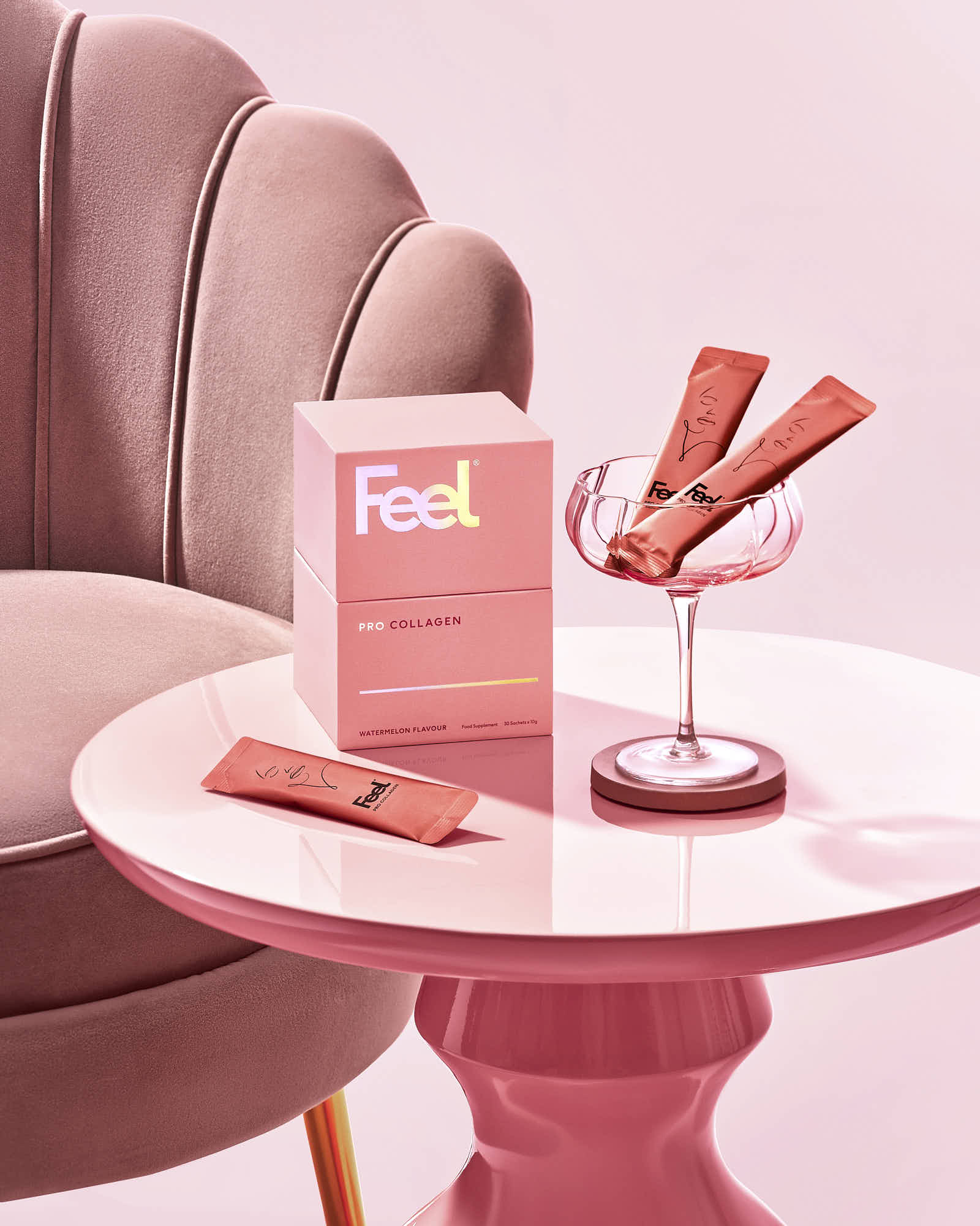 Feel Pro Collagen watermelon flavor product on pink table with soft chair and elegant drink glass.