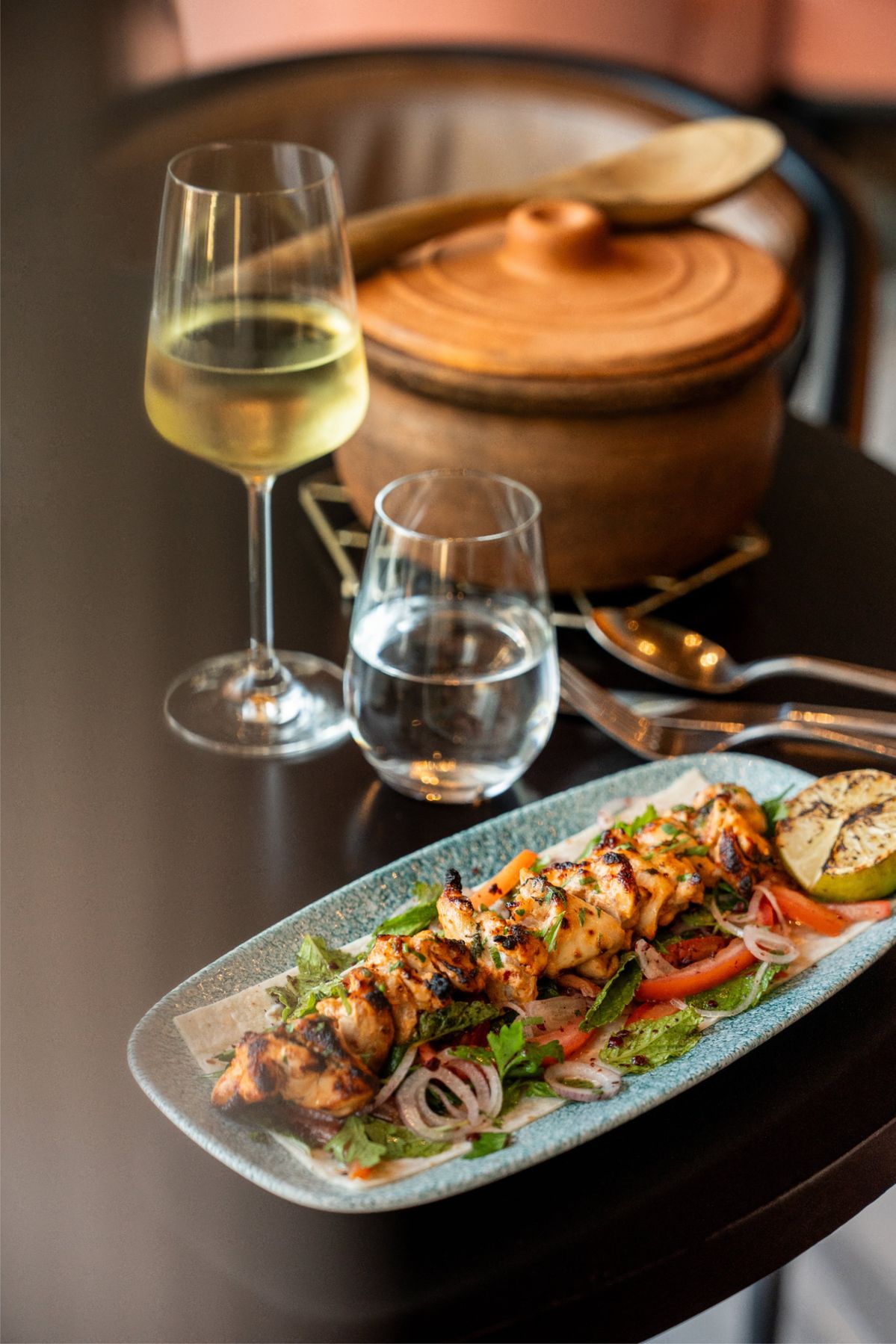 Char-grilled chicken skewers served with seasonal vegetables and wine, showcasing Dhoom’s farm-fresh sourcing and open-flame cooking techniques.