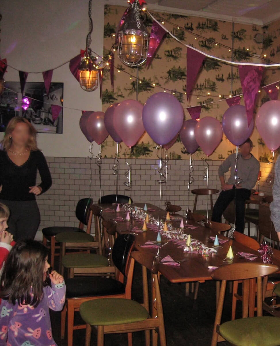 Large table with chairs in a room that is decorated with pink and purple baloons and streamers