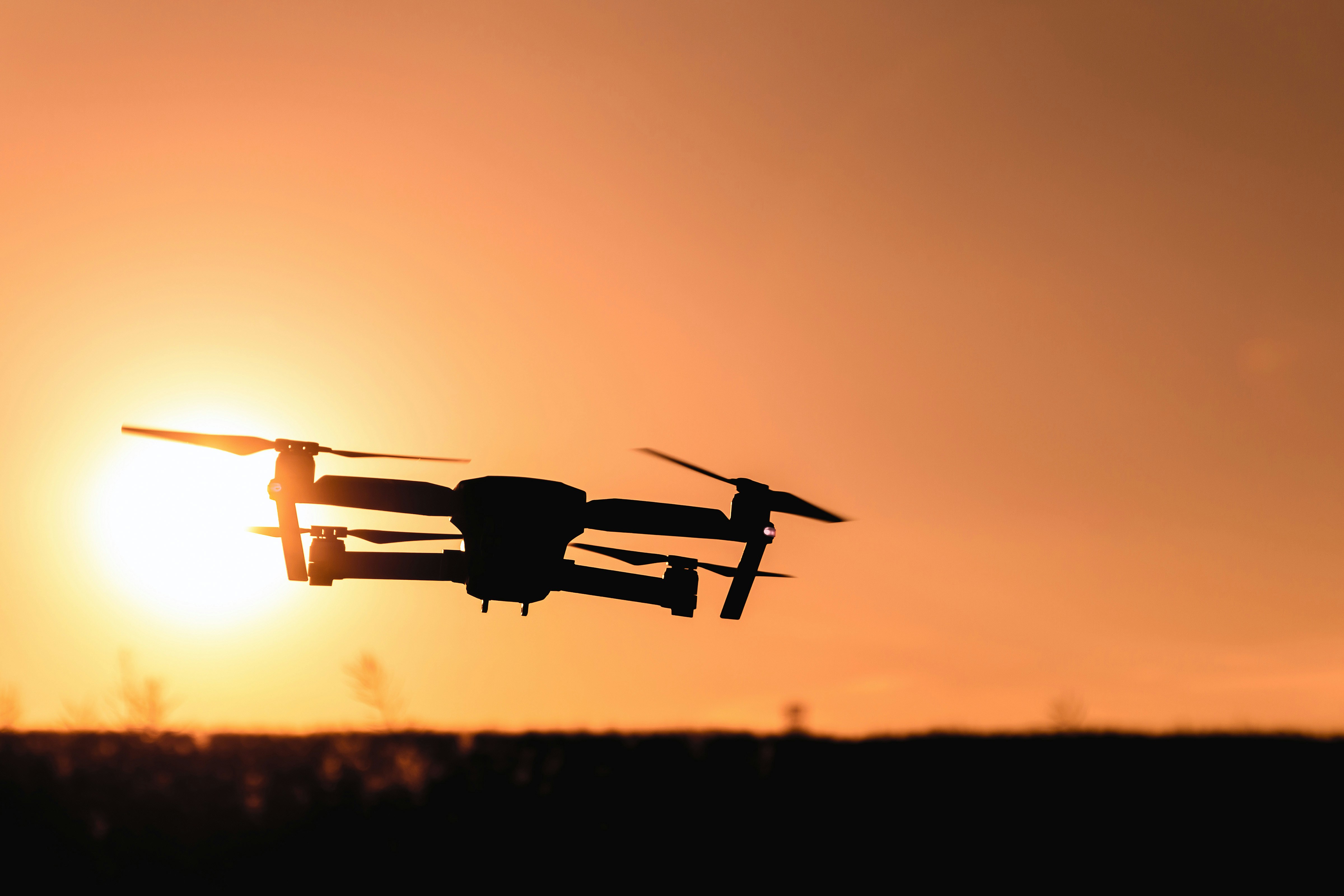A quadcopter drone flying over a field at sunset