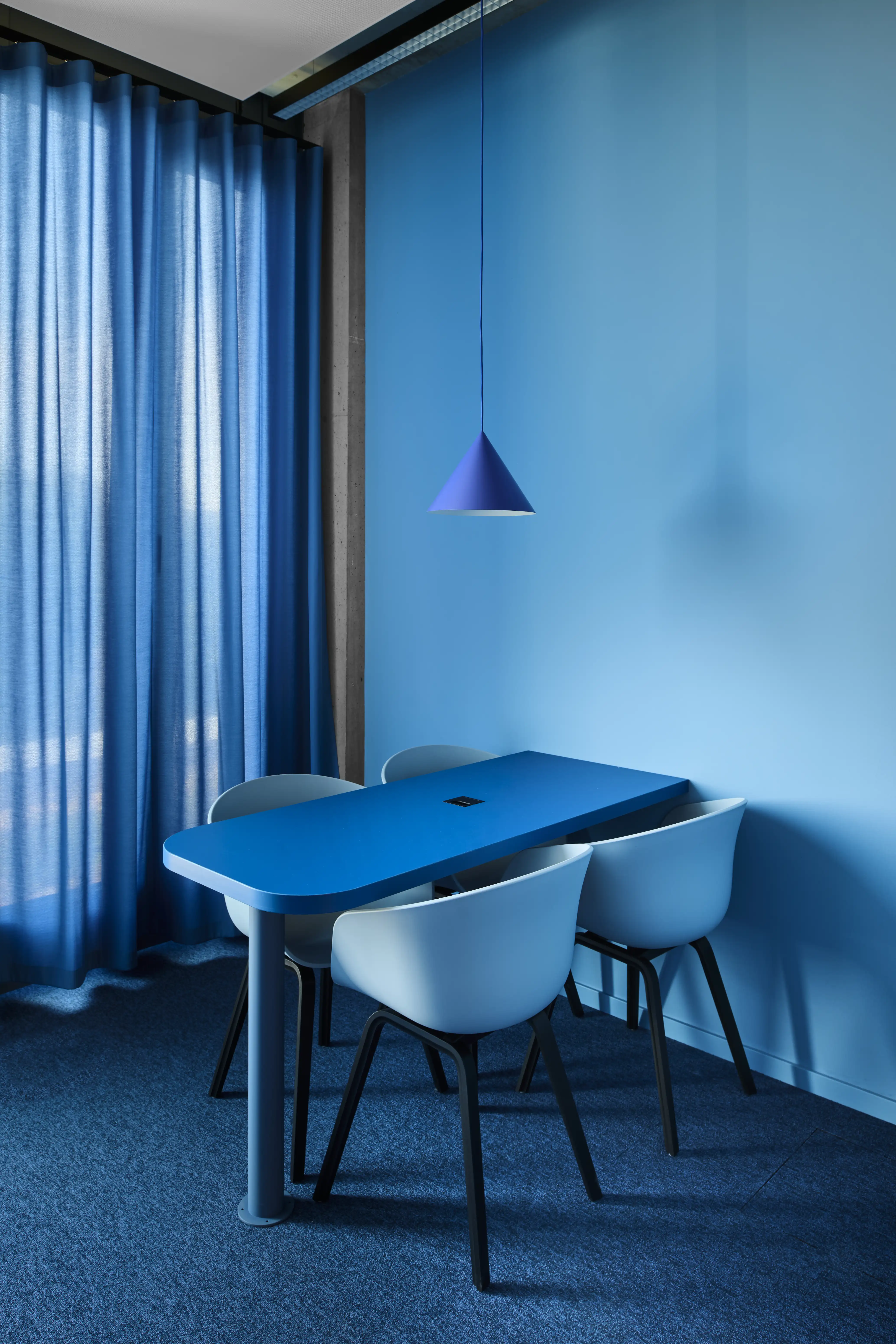 Monochrome blue meeting room at ENPAL with a cobalt table, light blue shell chairs, a blue cone pendant light, blue curtains and matching blue carpet.