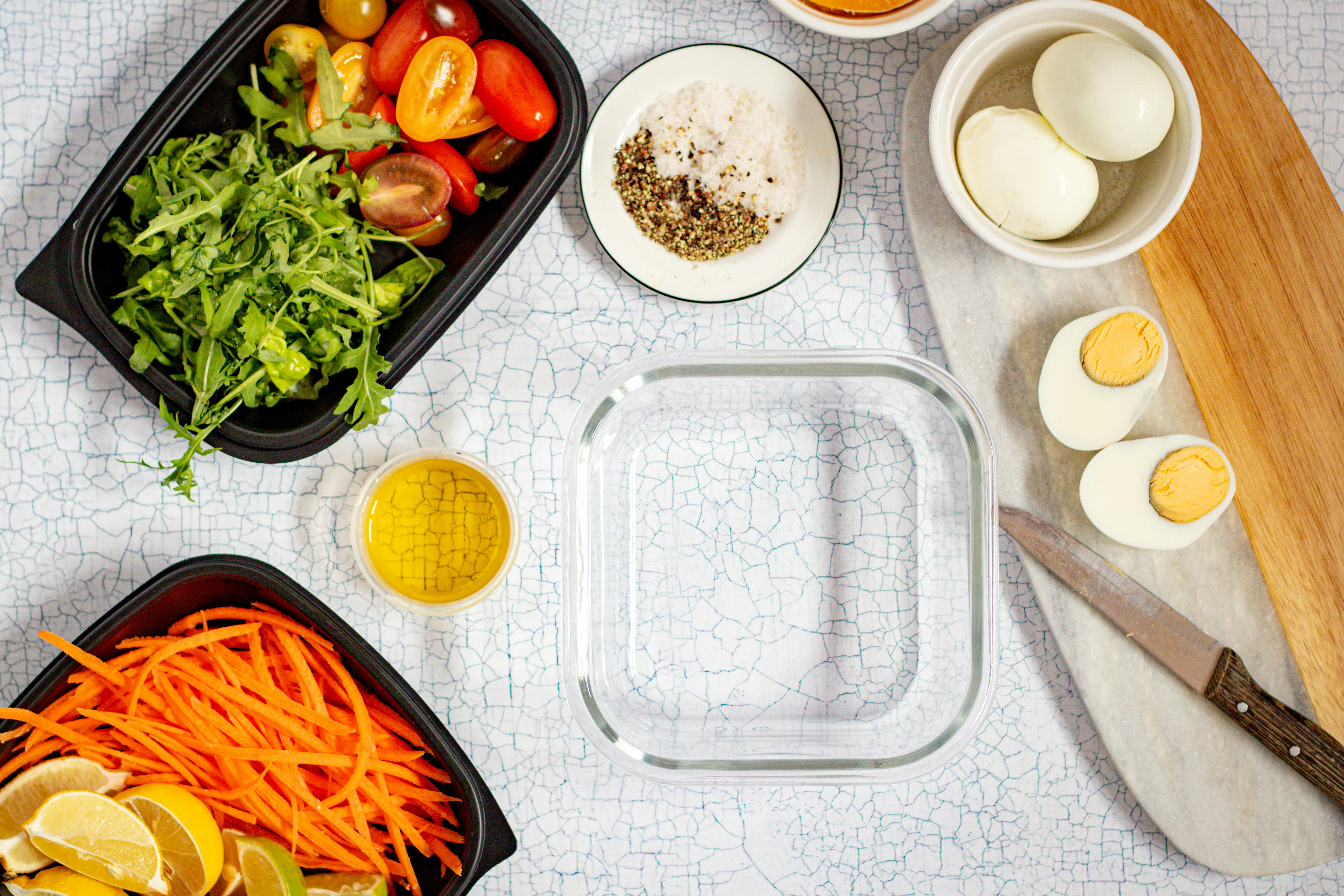 Meal prep ingredients with a glass container, plastic containers, and boiled eggs.