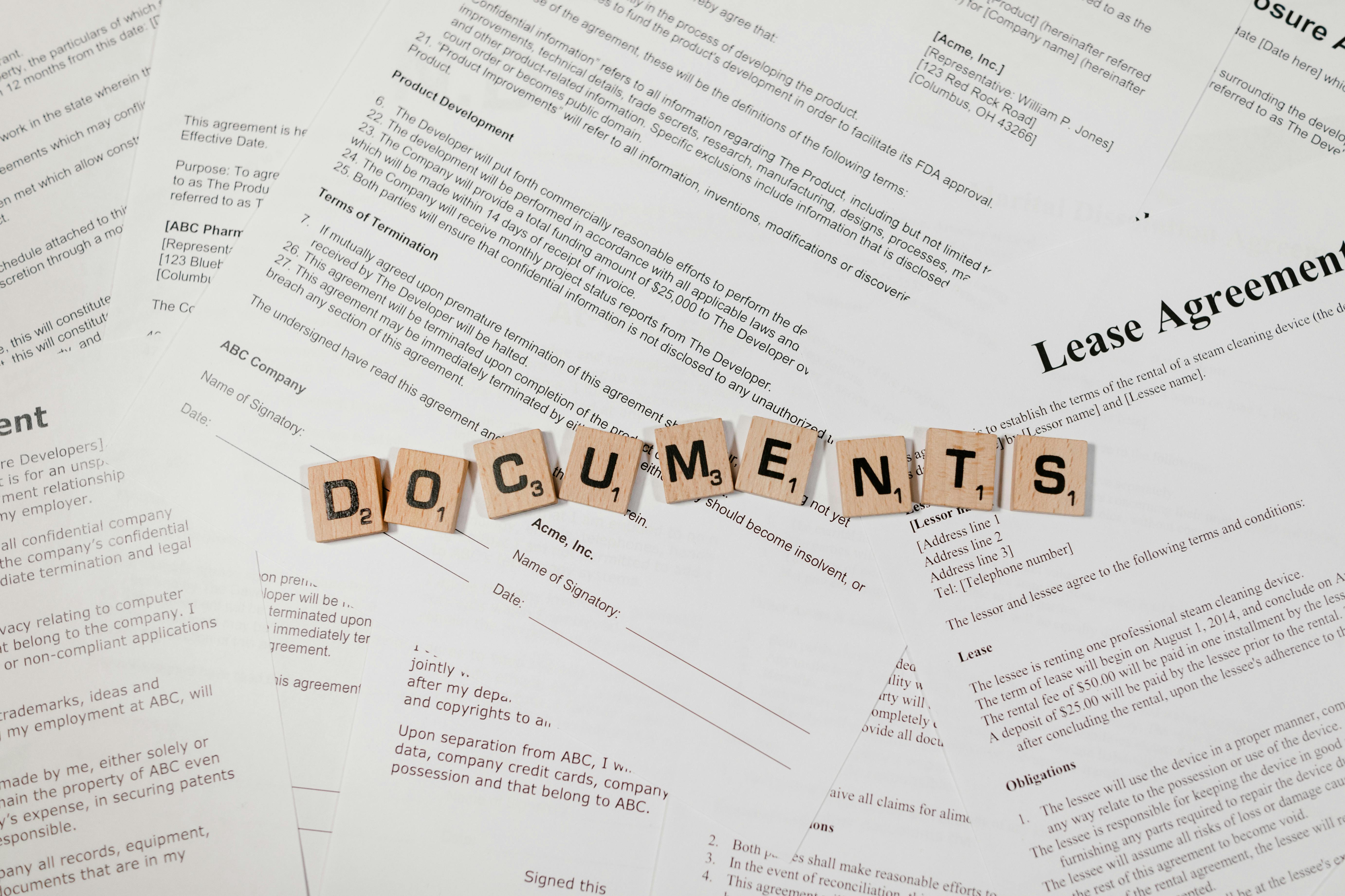 A spread of printed legal paperwork and contract pages, including a “Lease Agreement,” with wooden letter tiles spelling “DOCUMENTS” across the center. It looks like a desk setup for reviewing, organizing, or signing formal agreements.