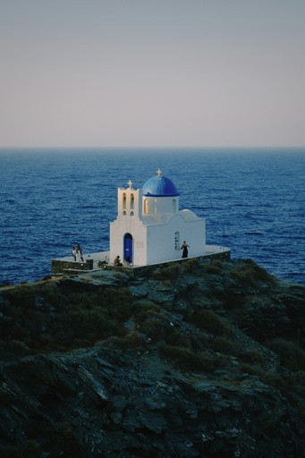 White church with blue dome on cliff overlooking ocean