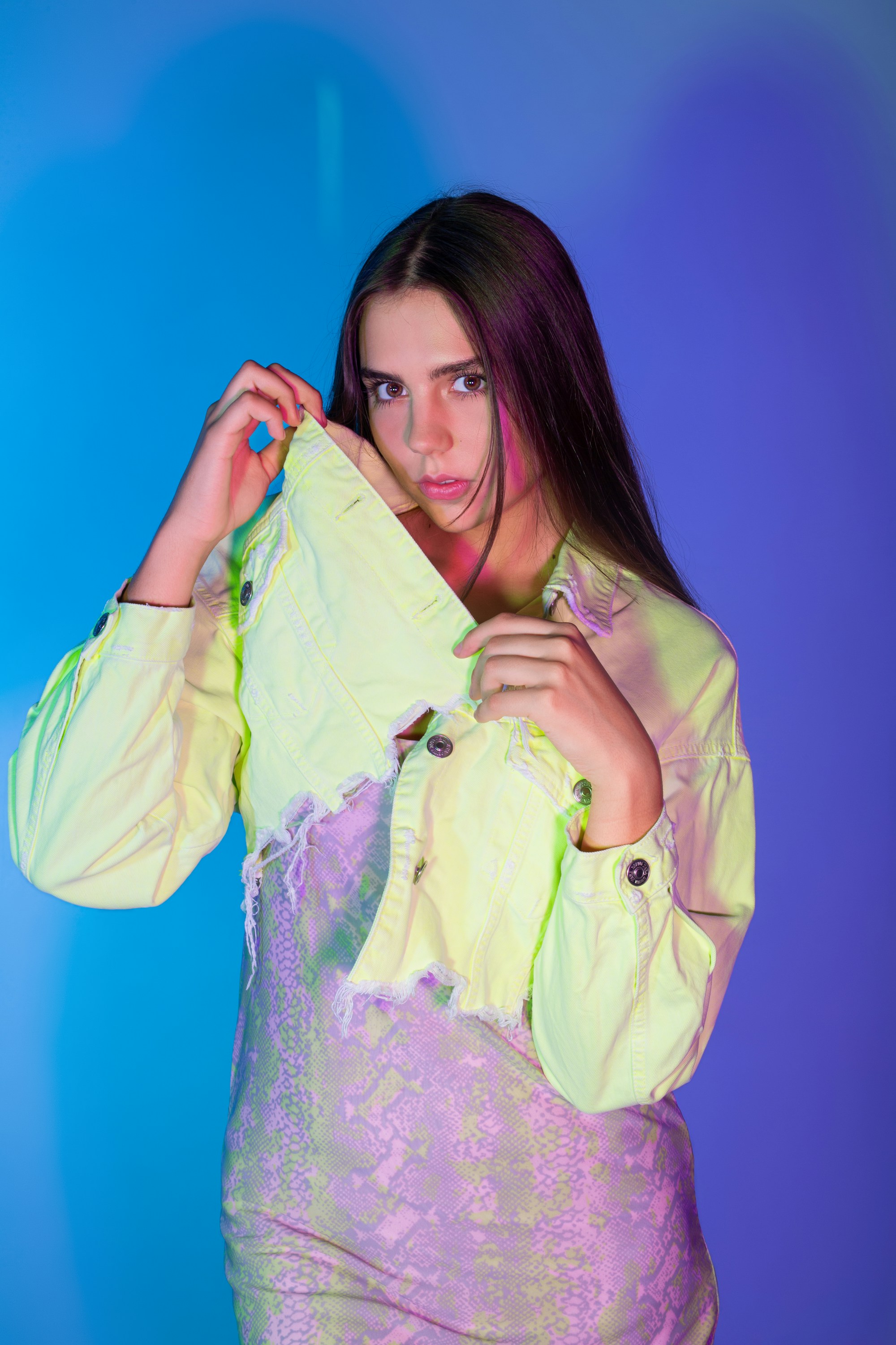Model holding the collar of a neon lime jacket under blue light