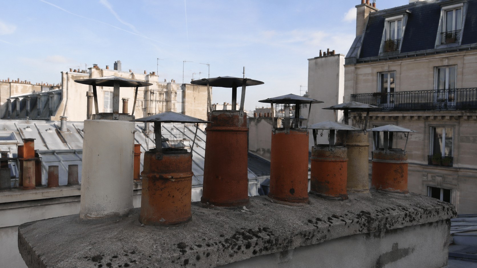 Photo réaliste de chapeaux de cheminée sur mitrons parisiens en toiture zinc à Paris, avec conduits anciens en terre cuite et bâtiments haussmanniens en arrière-plan.