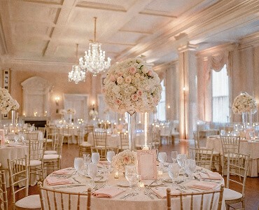 Elegant banquet hall with large chandelier, beautifully arranged tables, and soft lighting for an upscale event.