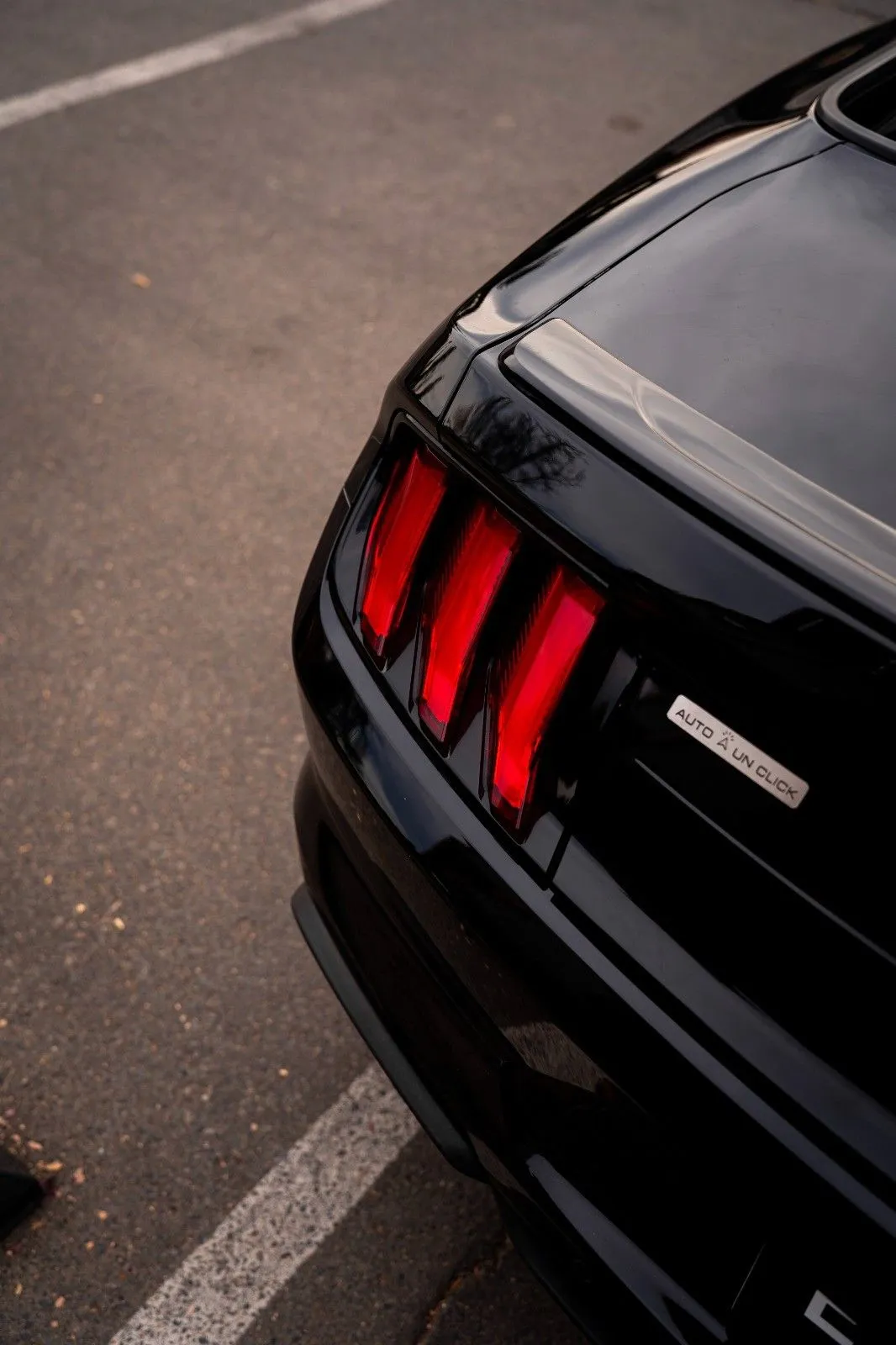 Detalle de focos traseros rojos del Ford Mustang negro con etiqueta Auto Link Check