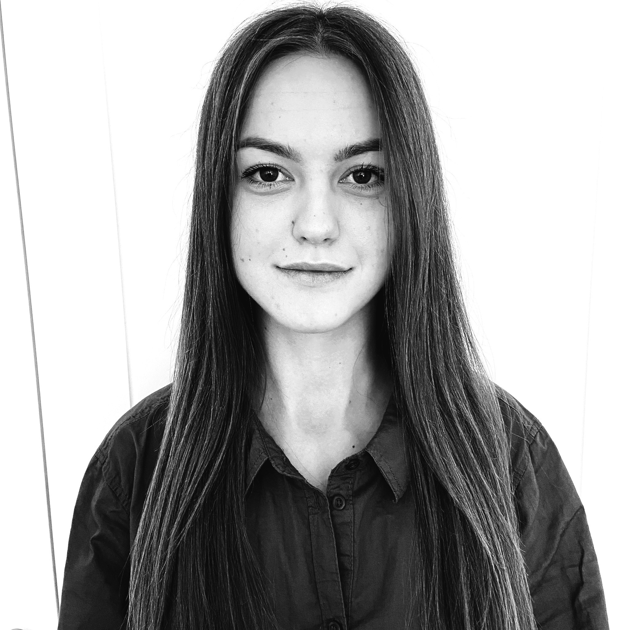 A woman with short curly hair wearing a black t-shirt looks into the camera.