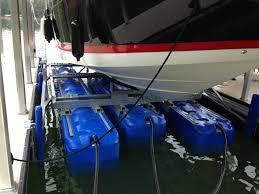 A boat is partially elevated from the water using a lift system with multiple blue pontoons, positioned in a marina setting.
