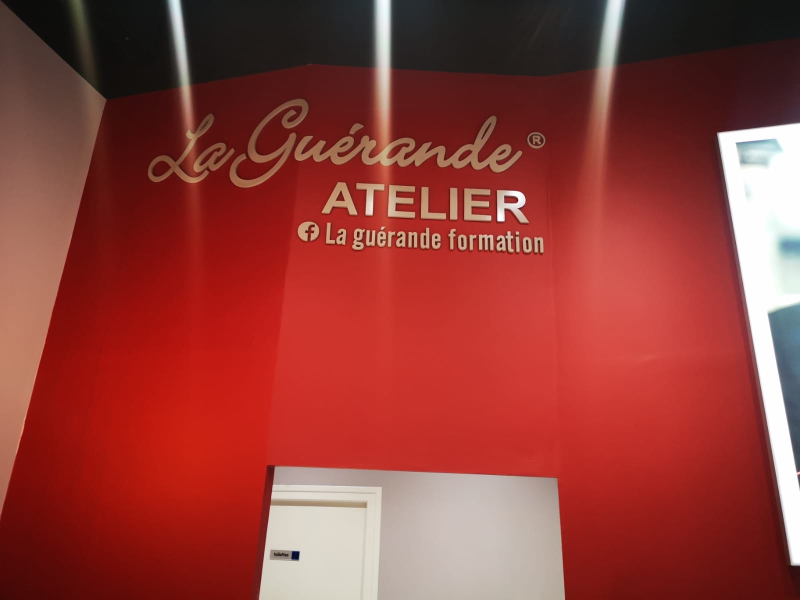 Mur rouge arborant le texte « La Guérande ATELIER » en caractères élégants et audacieux. Un éclairage lumineux et un design moderne créent une atmosphère accueillante.
