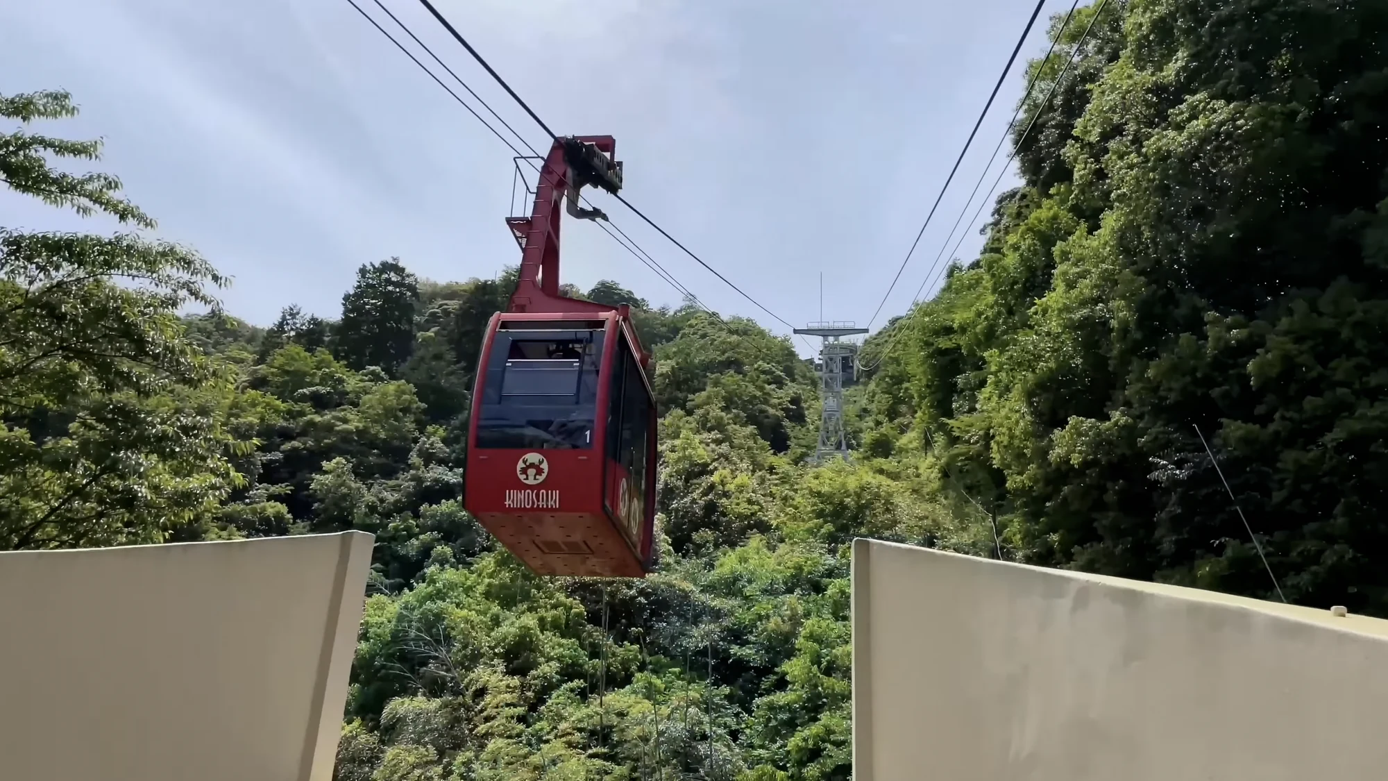 A red ropeway gondola climbing above forested hillside at Kinosaki.
