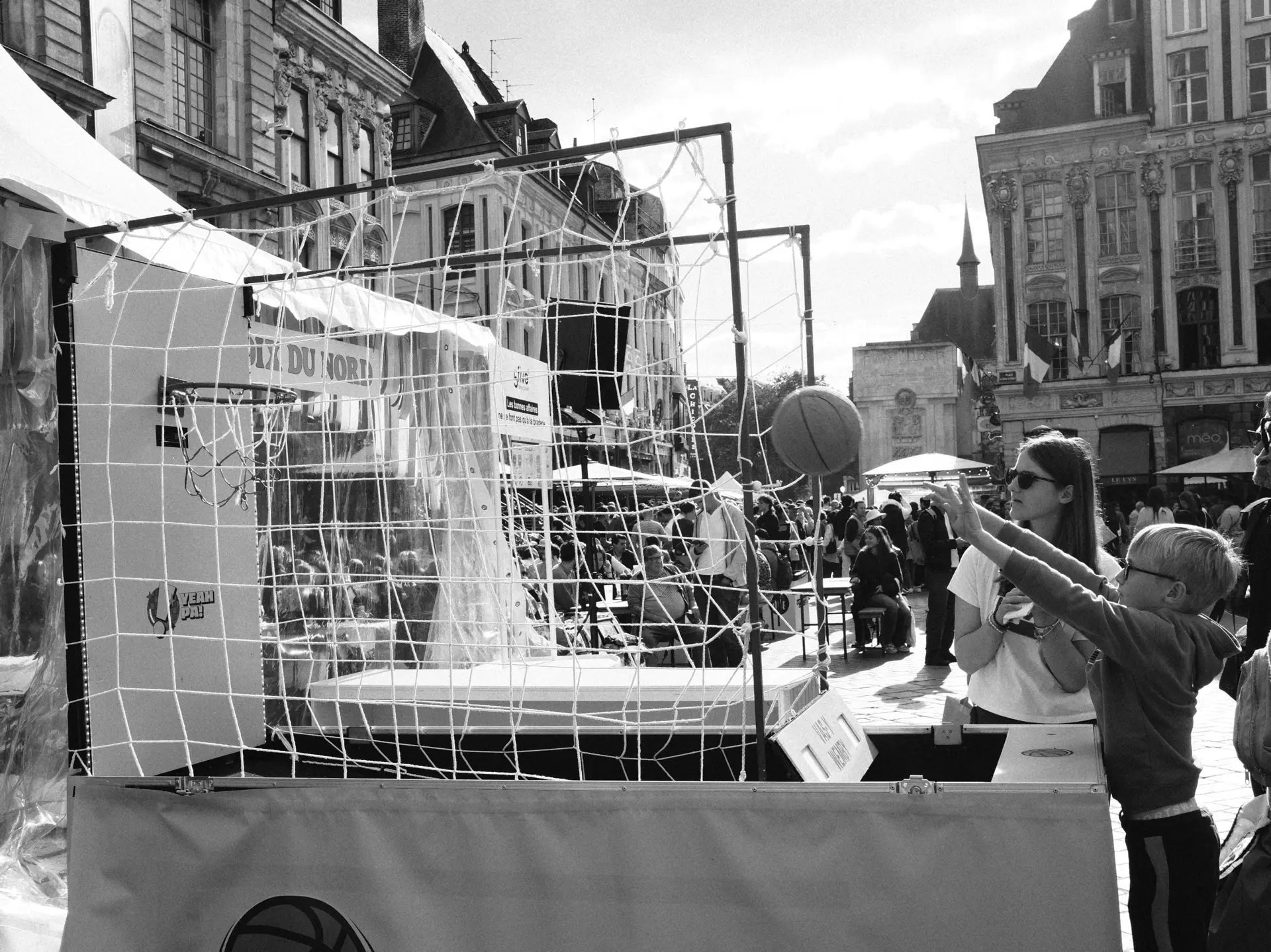 People browsing a stall with a netted frame, in black and white