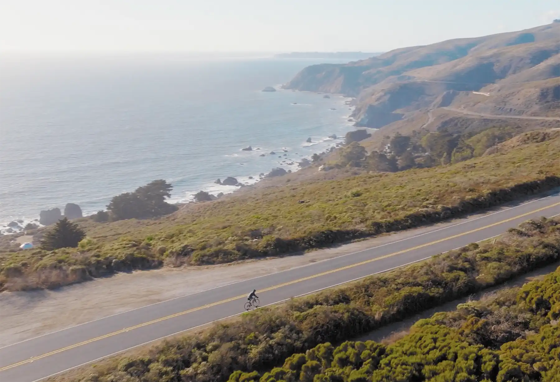 Cyclist riding along a coastal highway overlooking the Pacific Ocean.