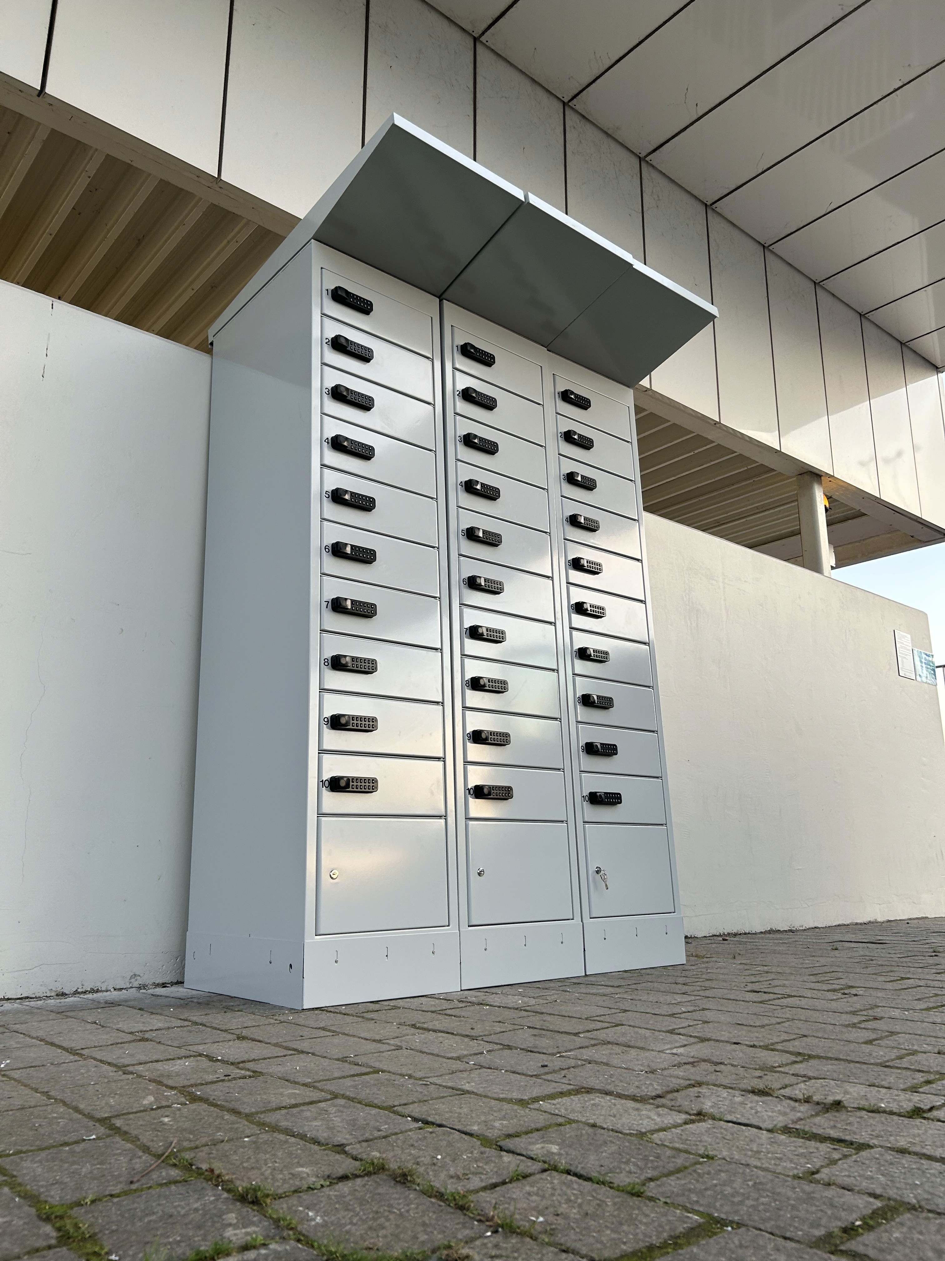 PowerShelter e-bike battery charging lockers installed outdoors, showing three units with numbered compartments and PIN locks.
