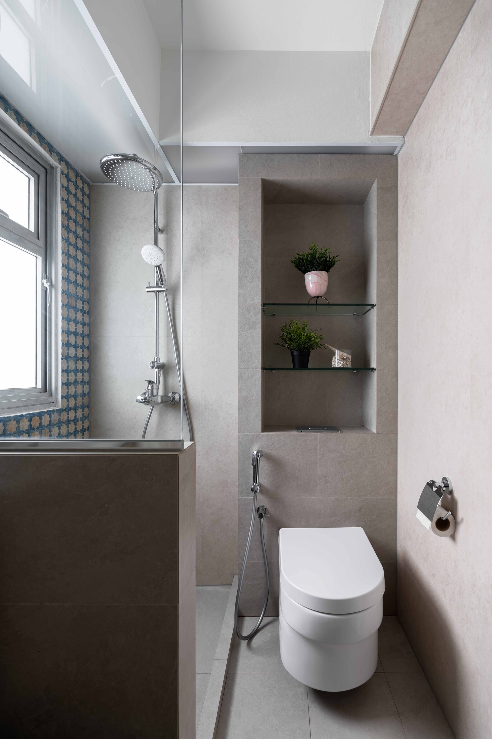 A modern bathroom featuring a toilet, sleek gray walls, and a shower with a glass door. Natural light enters through a window.