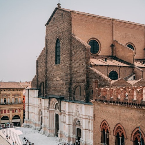 A large, historic brick church with a white and brown facade, located in a city square with people walking around.