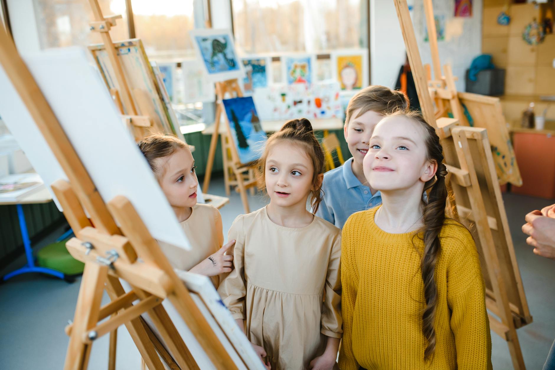 Three students work together on a large mural using finger paints and sponges on a long roll of paper.