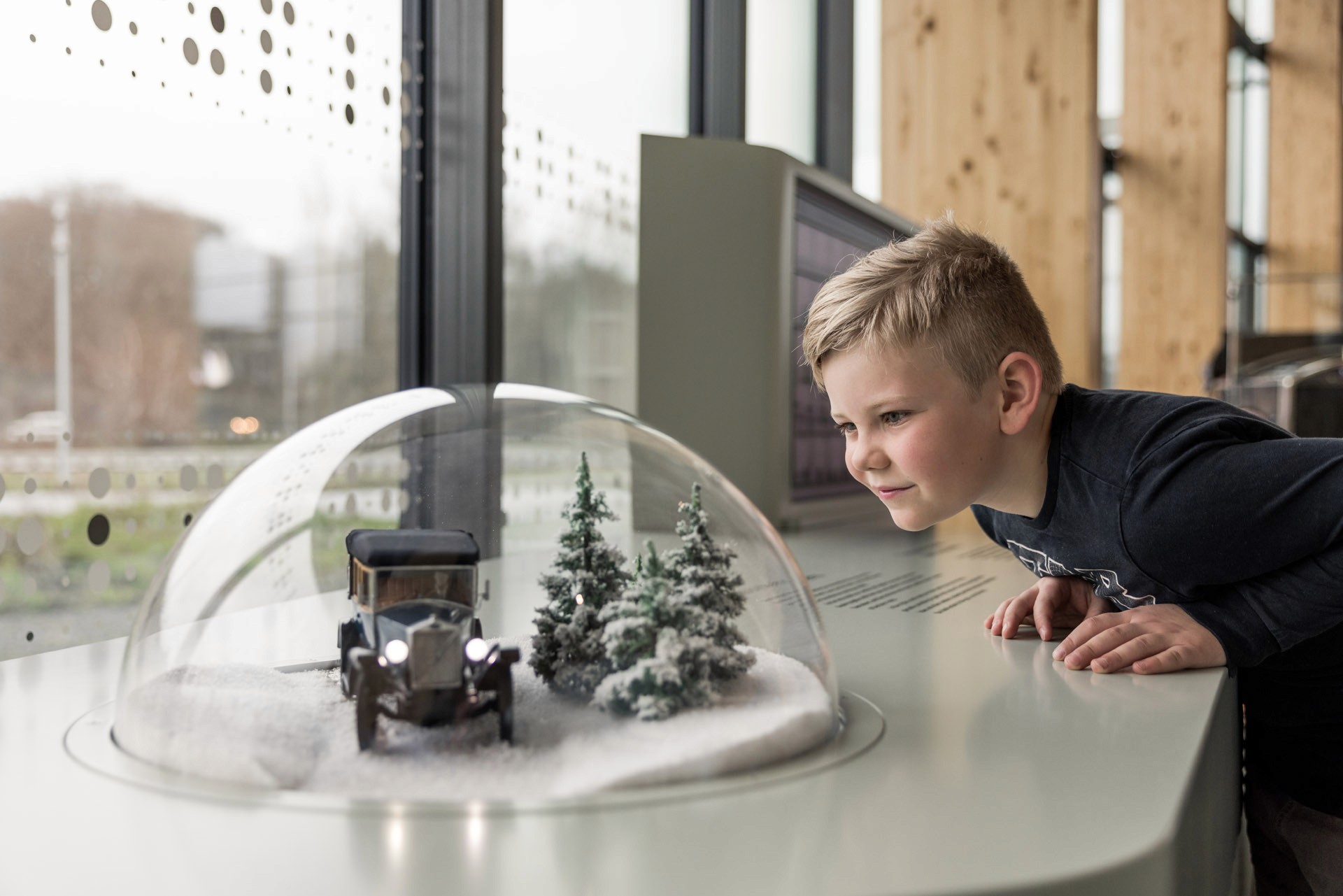 Ung pojke tittar på en gammal bil inuti en snöglob på World of Volvo