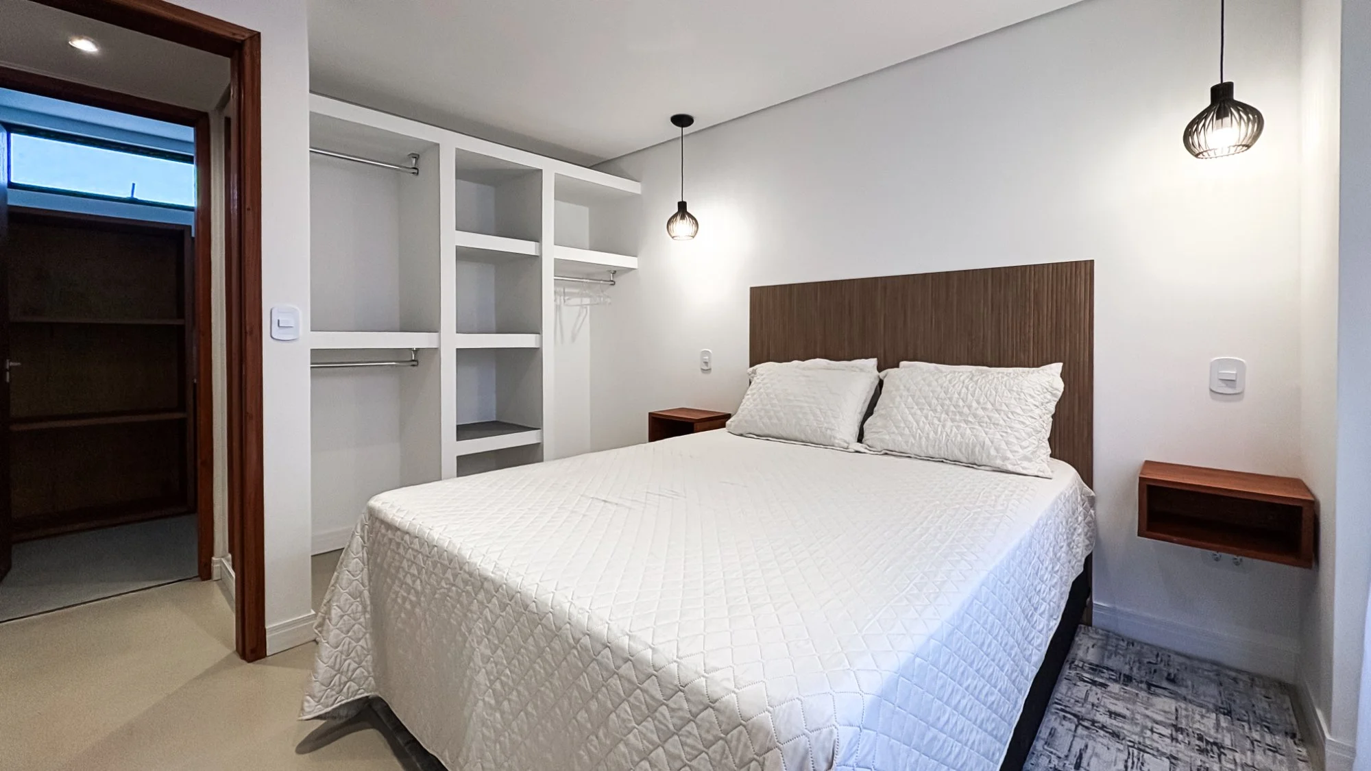 Modern bedroom with queen bed, wooden headboard, open closet, and pendant lighting