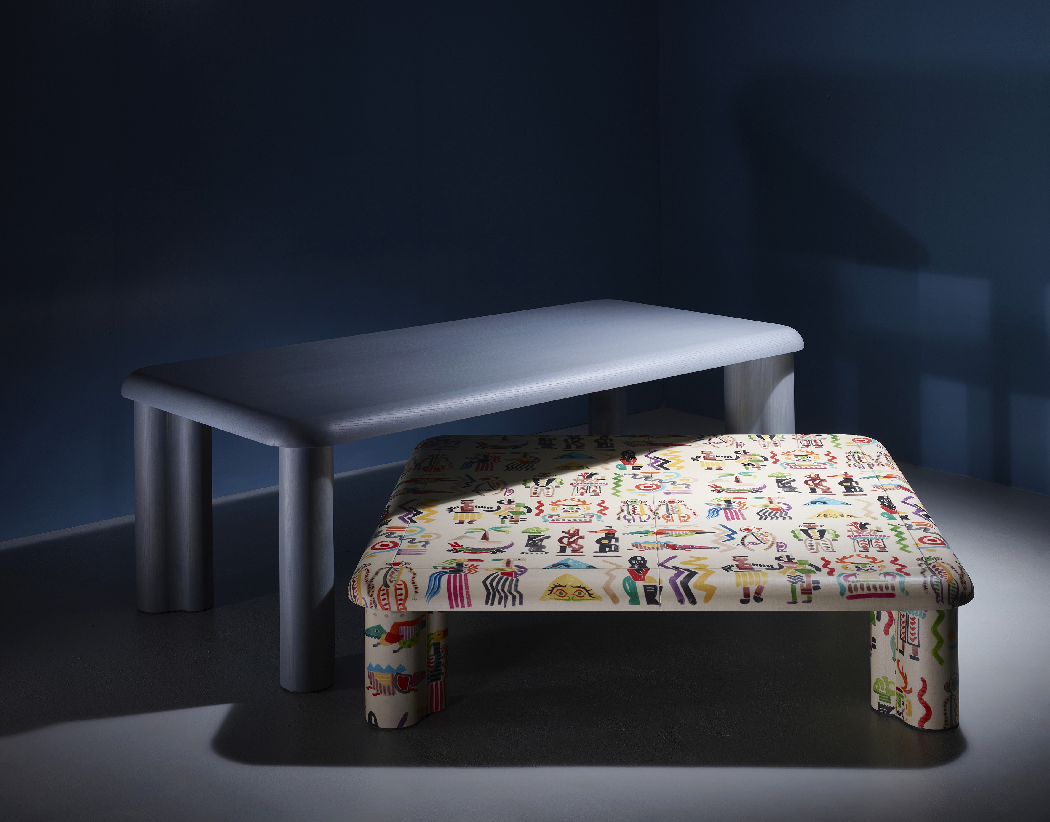 Modern tables set featuring a minimalist grey table and a low square table with a colorful tribal art pattern.