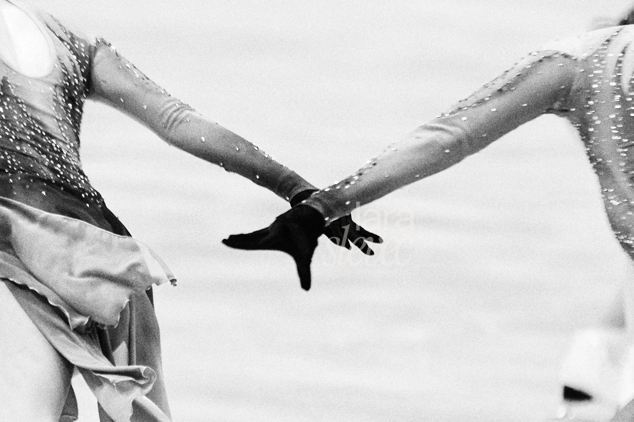 Schwarz-Weiß Bild im Analog-Stil. Detailaufnahme zweier Läuferinnen, die ihre Hände überkreuzen. Team Haydenettes. ISU Synchronized Skating Championships 2026 in Salzburg. Fotografiert von Lara Slevec.