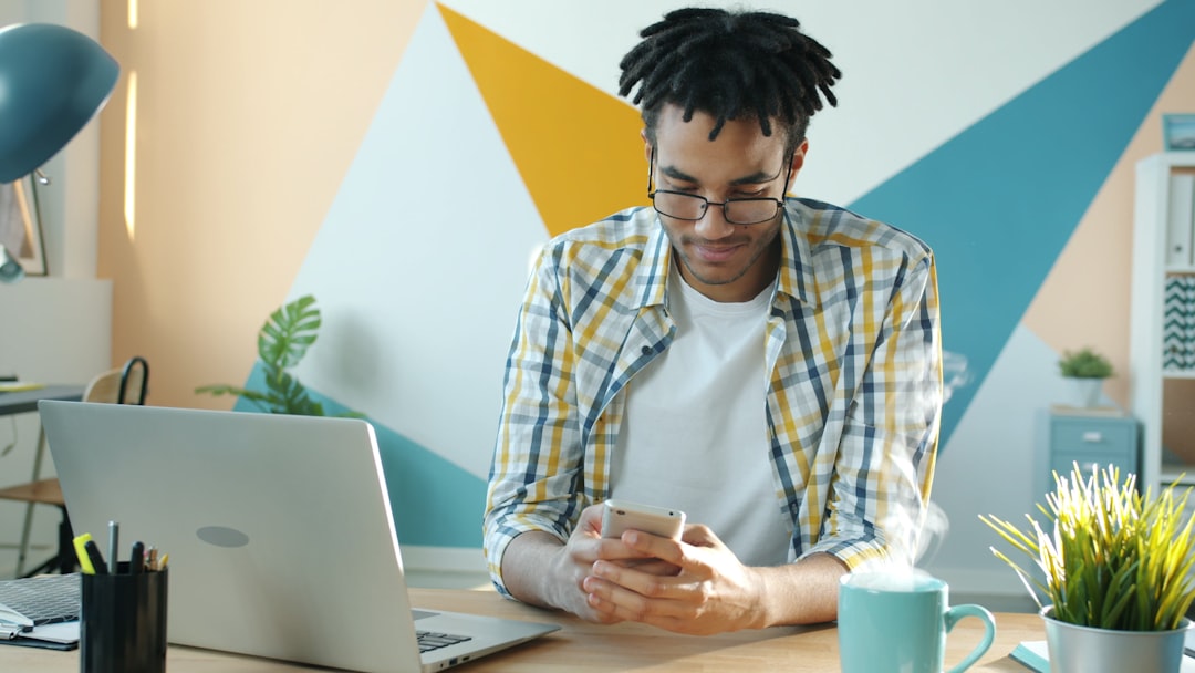 Man in plaid shirt using smartphone at desk