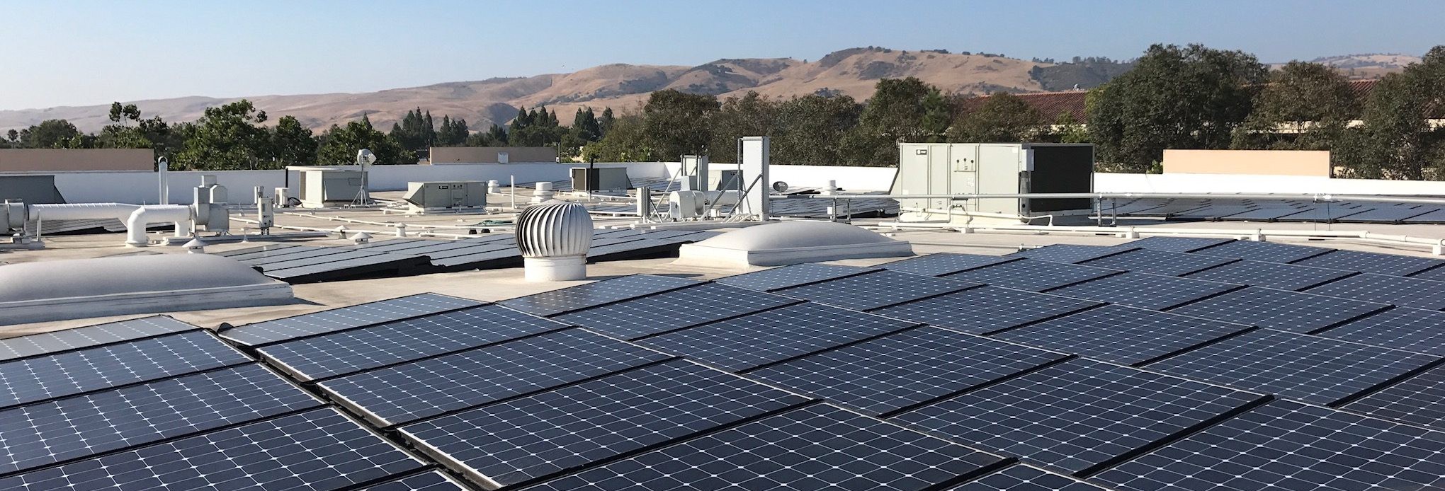 Rooftop solar panels under a clear sky, set against a backdrop of rolling hills and trees, convey a sense of sustainability and innovation.