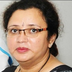 Smiling young woman with curly hair sitting at a laptop, in front of a teal wall.