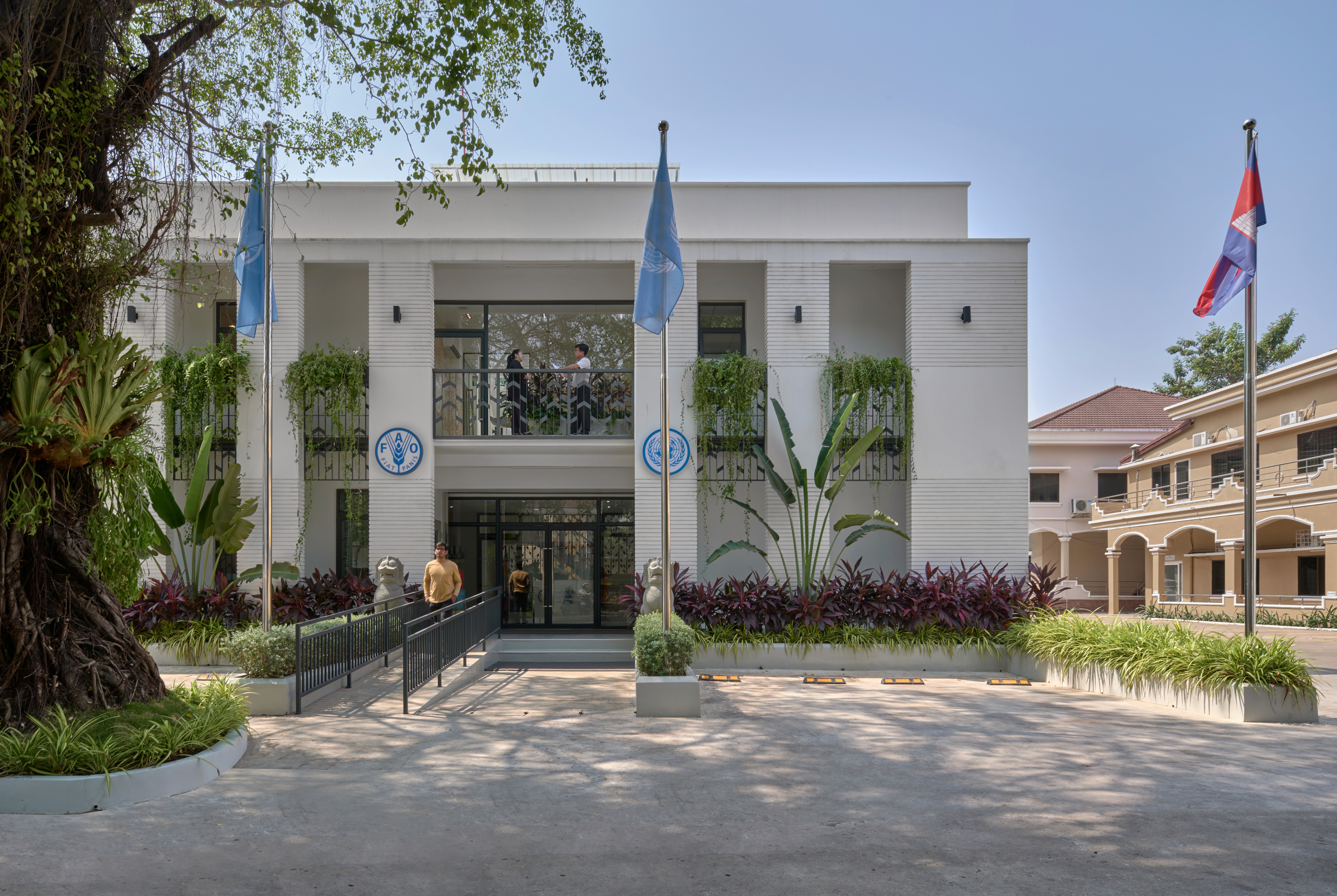 Symmetrical building facade of a modern workplace featuring integrated balcony planters with hanging vines and a central glass entrance.